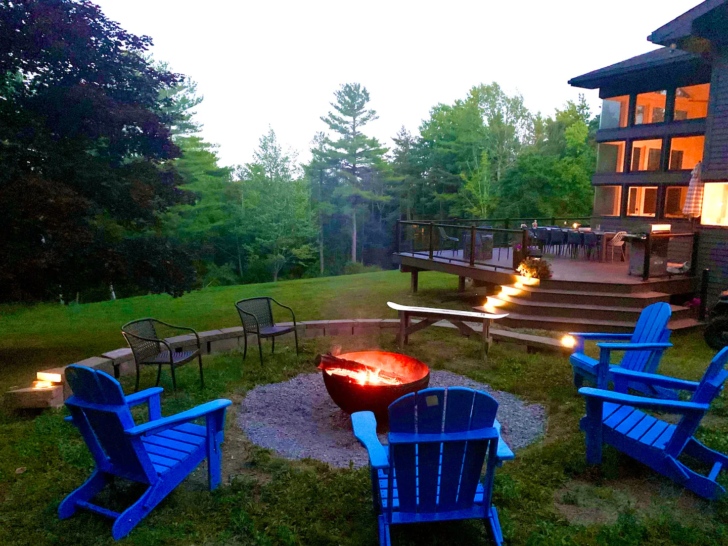 Two firepits and blue Adirondack chairs behind the house